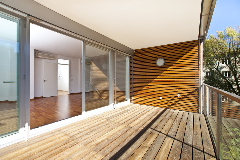 architectural contemporary - sunlit balcony with wooden floor and wall of an apartment building in green area.