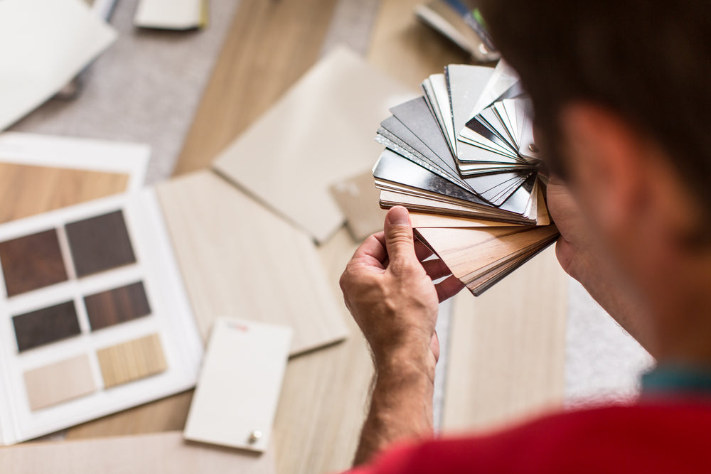 An individual carefully selecting the right wooden wall panels for his home. The man is holding a sample of wood paneling and examining its color and texture, surrounded by various other samples on display.